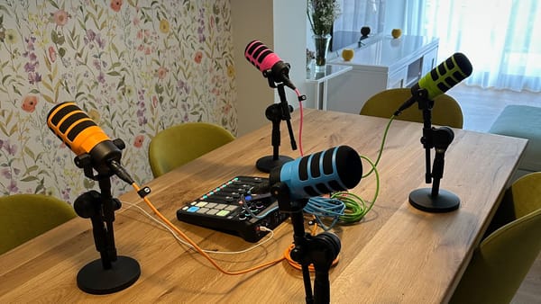 Una RØDECASTER PRO II y cuatro micrófonos RØDE PodMic, montados en pies de micro con los cables y los protectores en sus colores correspondientes rosa, verde, azul y naranja.